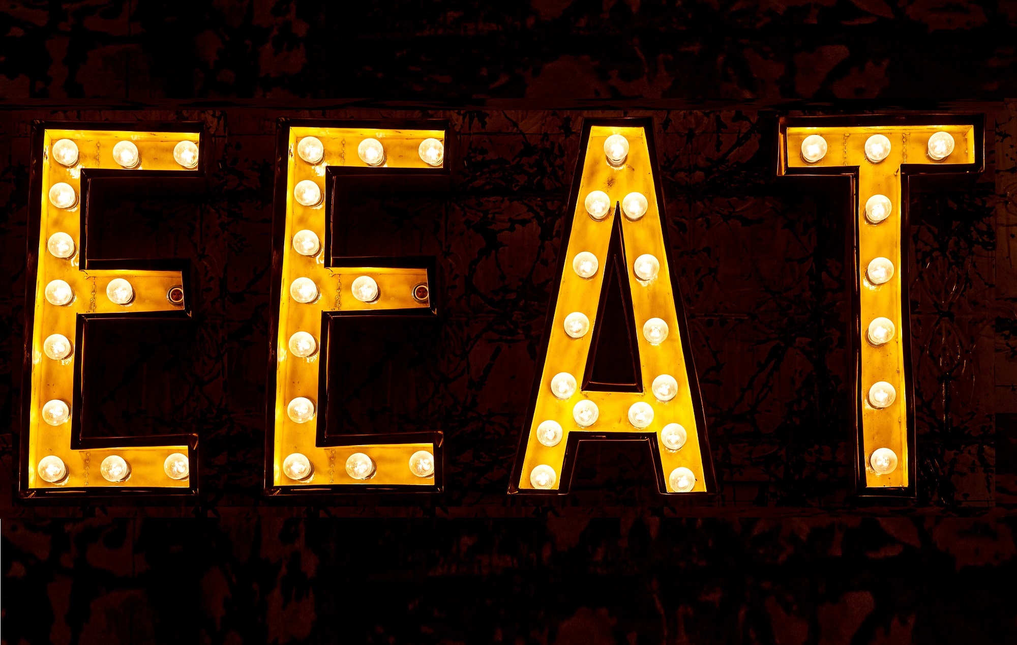 The word "eat" written by light bulbs, like a street sign, however it's spelled with two e's (E-E-A-T), which is an acronym for Experience, Expertise, Authority, and Trust.
